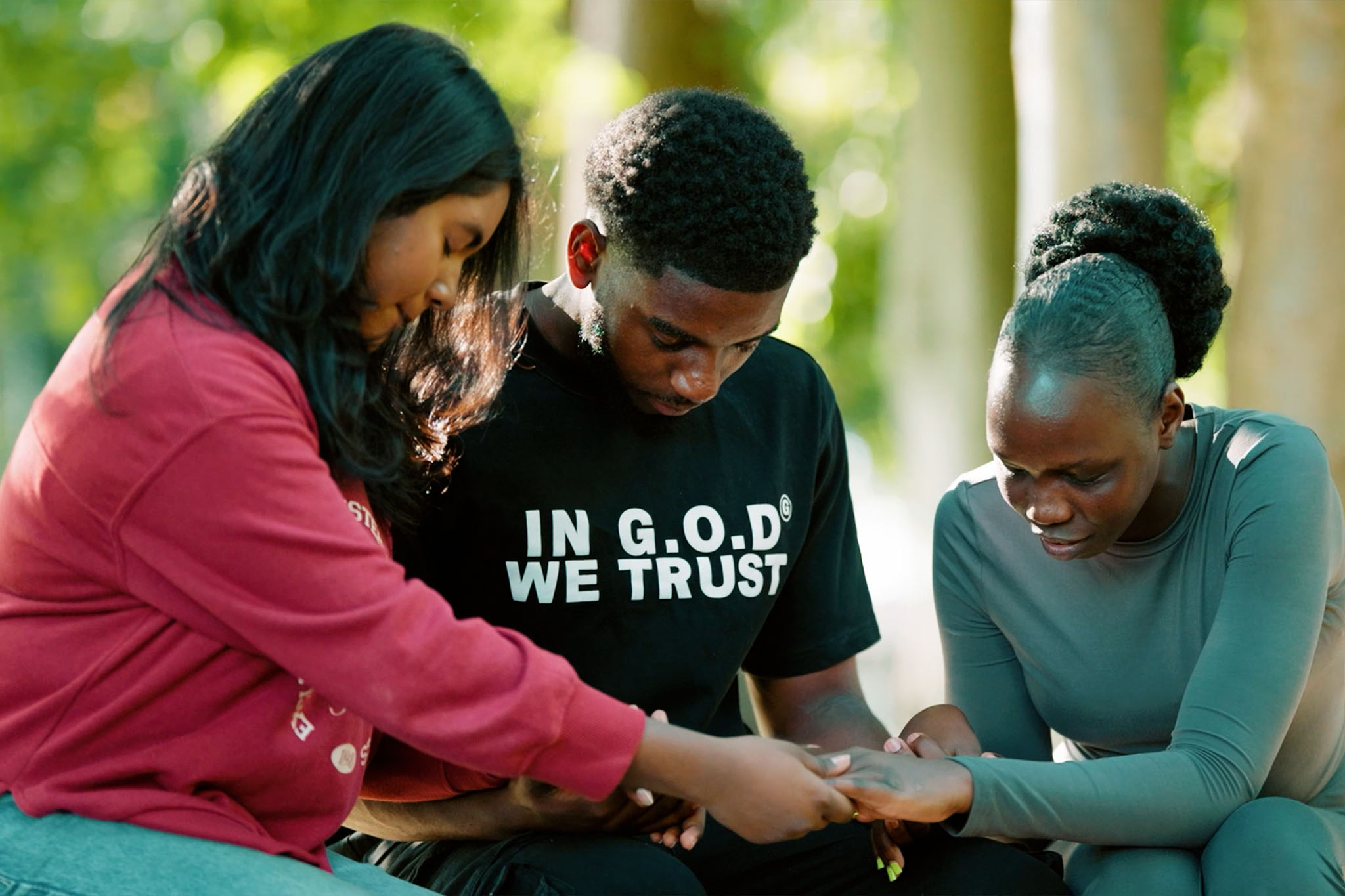 Three Newbold students sitting closely with hands joined in prayer